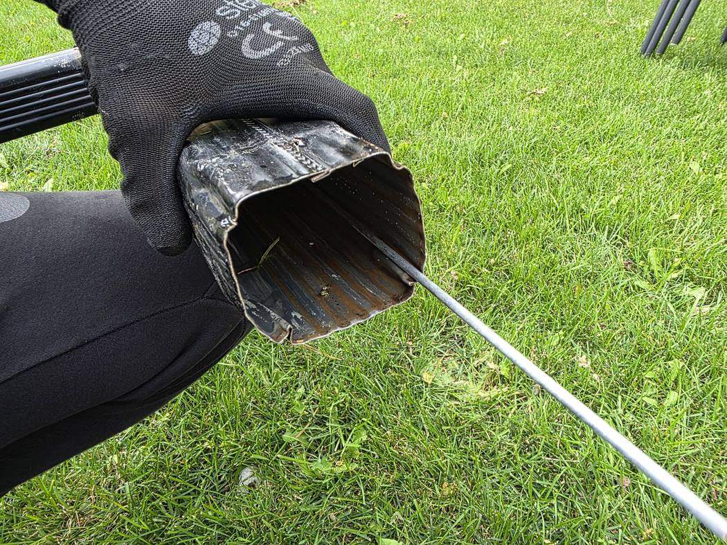 DT Cleaning technician holding a downspout section over a Toronto lawn with a rod run through it