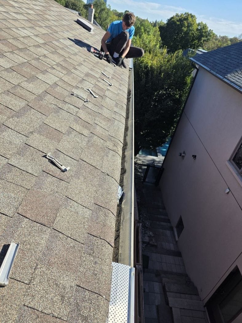 Eavestrough repair Etobicoke: leaf guards off, one panel still on in front, dark sediment along the trough and gutter brackets on the shingles