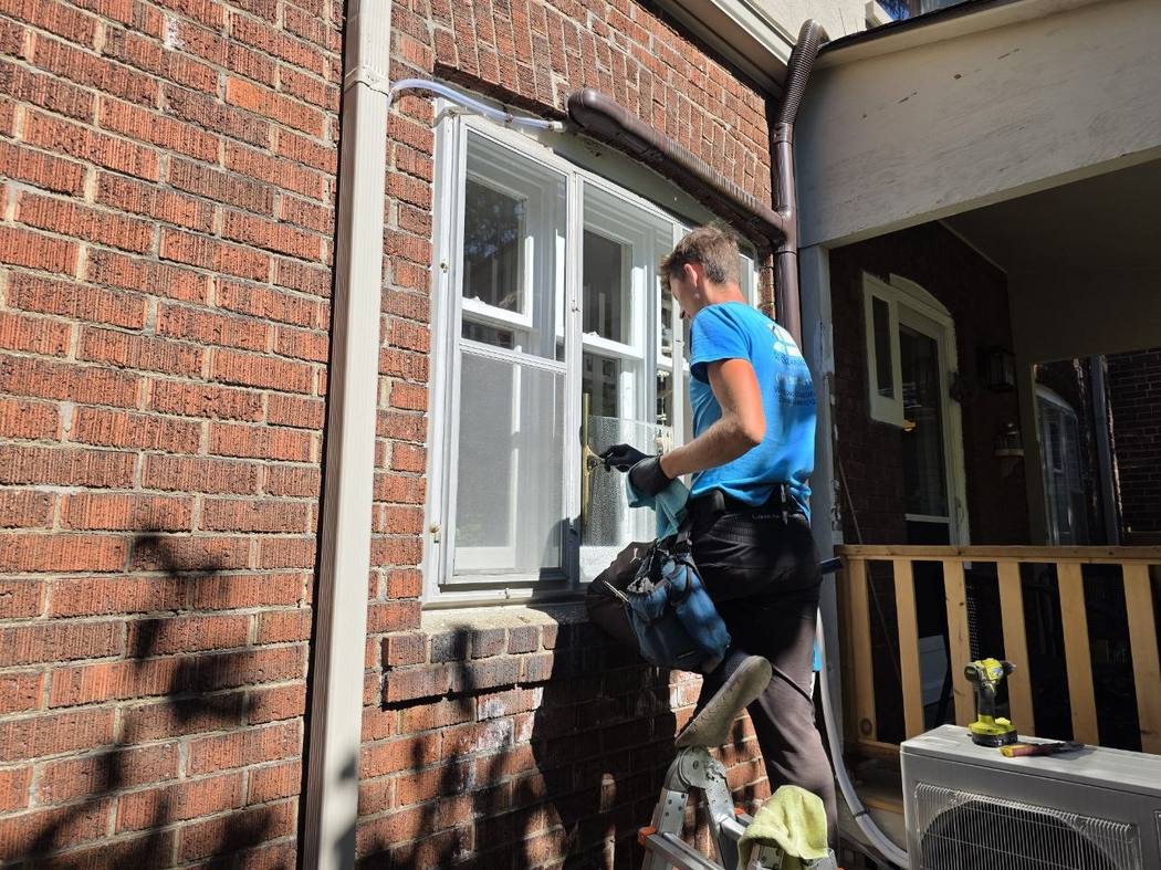 Washing the glass with a squeegee, Etobicoke Storm window cleaning Toronto: a DT Cleaning technician holding a brass squeegee against soapy glass on a brick house in Etobicoke