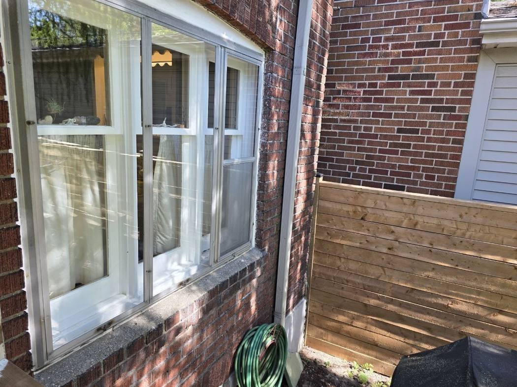 Metal storm frame over a three-part window, Etobicoke Storm window cleaning Toronto: a three-part window behind a metal storm window frame on a brick house in Etobicoke