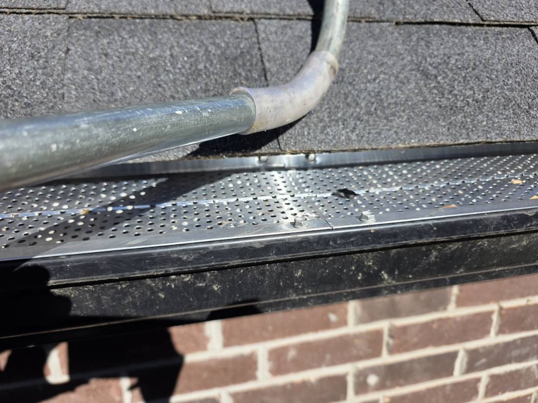 New aluminum gutter guard screwed to the eavestrough lip, North York Close-up of a perforated aluminum gutter guard fastened with hex-head screws to the front lip of a black eavestrough, North York