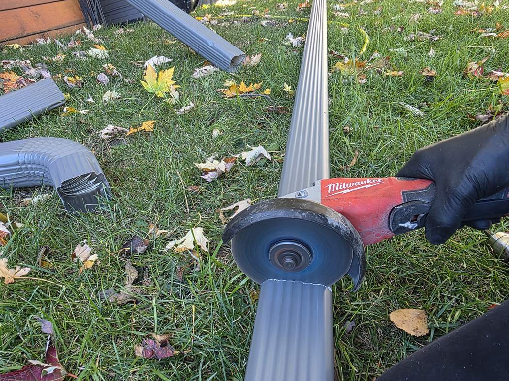 Cutting the new downspout with an angle grinder, Etobicoke Downspout installation Etobicoke: a red angle grinder over a new grey corrugated downspout on the grass, elbows nearby