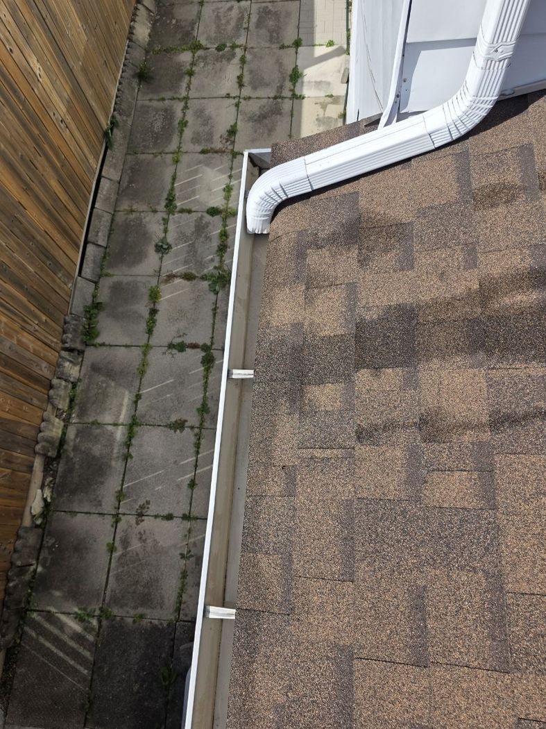 A white downspout from an upper wall running across the shingles into the eavestrough corner, Mississauga