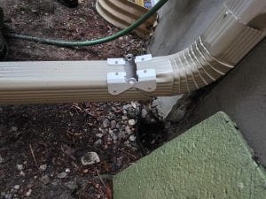 Downspout repair Etobicoke: a hinged aluminum downspout extension at ground level beside the foundation of a house, October 2026