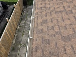 Eavestrough repair Mississauga: a long straight run of white eavestrough with evenly spaced brackets along a shingle roof above a fenced walkway, October 2026