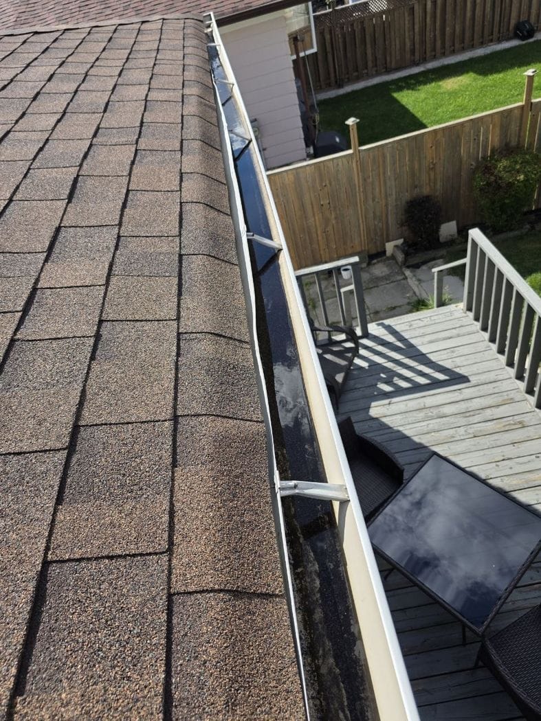 Eavestrough repair Mississauga: dark water and dirt lying in the eavestrough at the roof edge above a wooden deck and patio table