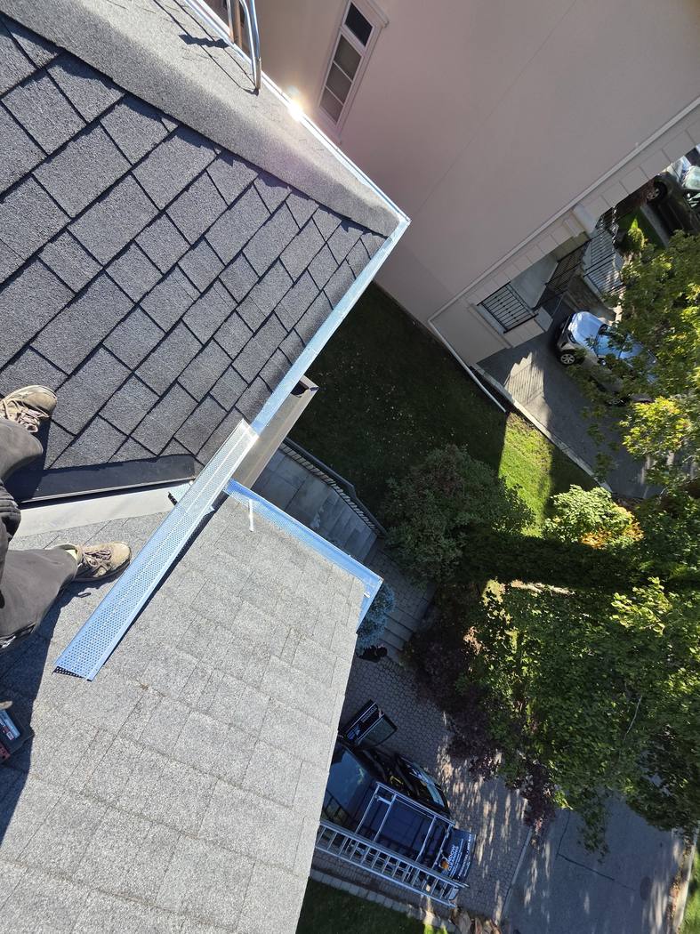 Fitting new aluminum gutter guards at a roof corner, North York Gutter guard replacement North York: new perforated aluminum guard sections fitted at an outside corner of the eavestrough, the work truck far below