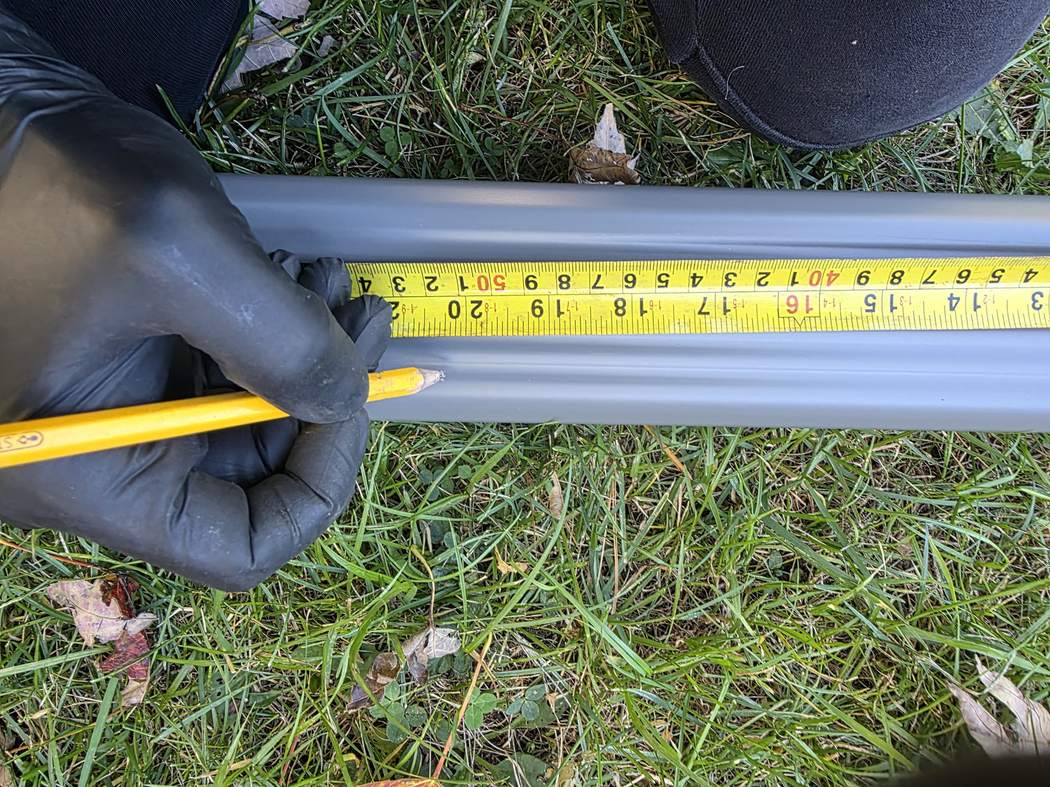 Measuring the new downspout, Etobicoke Downspout installation Etobicoke: gloved hands measuring a new grey downspout with a tape measure and marking it with a pencil