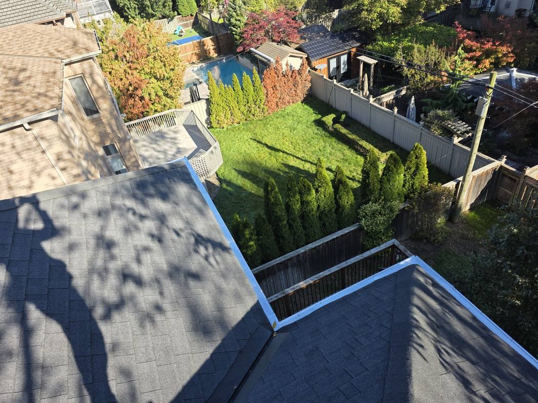 New gutter guards where two roof sections meet, North York Gutter guard replacement North York: new white perforated guards along two roof sections meeting at a valley above a fenced backyard