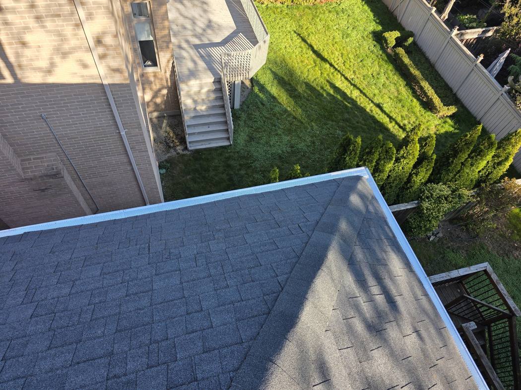 New gutter guard along a hip roof edge, North York The new white perforated gutter guard along the edge of a hip roof above a deck and a fenced lawn in North York